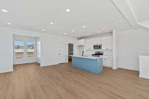 Two tone kitchen with open floor plan, a center island with sink, light wood-style flooring, stainless steel appliances, and recessed lighting