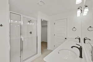 Bathroom with a shower stall, double vanity, a walk in closet, and light tile patterned floors