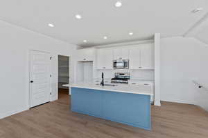 Kitchen with light wood-type flooring, a kitchen island with sink, stainless steel appliances, dual tone cabinets, and tasteful backsplash