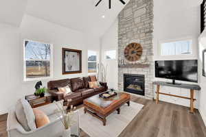 Living area with vaulted ceiling, wood finished floors, a stone fireplace, ceiling fan, and recessed lighting