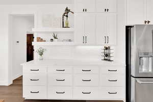 Kitchen with stainless steel fridge, open shelves, white cabinets, light stone counters, and light wood-style flooring