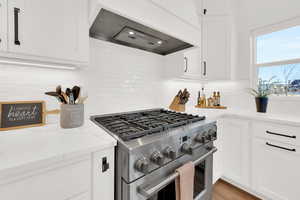 Kitchen with stainless steel gas range, light stone counters, white cabinets, backsplash, and recessed lighting