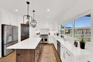 Kitchen featuring high quality appliances, light stone counters, a center island, light wood-style flooring, and two tone cabinetry