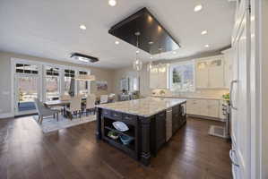 Two tone kitchen featuring glass fronted cabinets, two tone cabinetry, open shelves, backsplash, and light stone counters