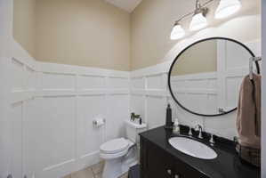 Half bathroom with vanity, a decorative wall, a wainscoted wall, and light tile patterned flooring