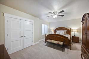 Bedroom with a textured ceiling, light carpet, a ceiling fan, and a closet