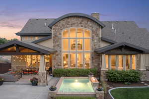 Back of house featuring stone siding, a hot tub, a shingled roof, and a patio