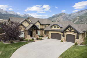 View of front of property featuring a front yard, a mountain view, concrete driveway, and stone siding