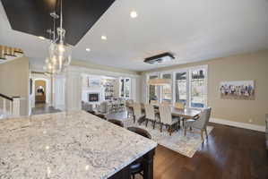 Kitchen with pendant lighting, light stone countertops, dark wood-style floors, a warm lit fireplace, and a kitchen breakfast bar