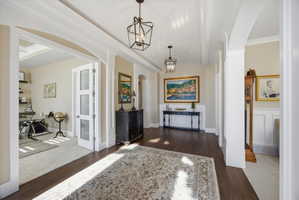 Corridor with dark wood finished floors, arched walkways, hanging lights, a barrel ceiling, and ornamental molding
