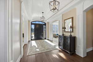 Foyer entrance featuring arched walkways, a barrel ceiling, hanging lights, and dark wood-style floors