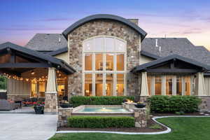 Back of house at dusk with stone siding, board and batten siding, and a patio
