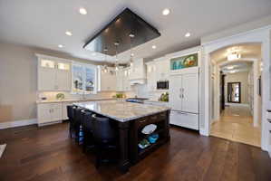 Two tone kitchen with light stone countertops, arched walkways, open shelves, glass insert cabinets, and two tone cabinetry