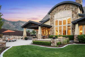 Back of property at dusk featuring stone siding, a patio area, a chimney, and a mountain view