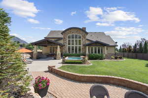 Back of property with french doors, a patio area, stone siding, a fenced backyard, and roof with shingles