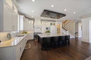 Two tone kitchen with glass insert cabinets, dark wood finished floors, stainless steel appliances, light stone counters, and decorative light fixtures