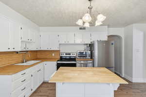 Kitchen featuring arched walkways, stainless steel appliances, a chandelier, white cabinetry, and light wood-style flooring