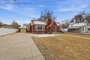 View of front of house with an outdoor structure, a chimney, brick siding, a detached garage, and concrete driveway