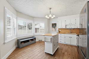 Kitchen with high end fridge, light wood-style floors, hanging lights, backsplash, and white cabinetry