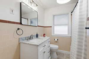 Bathroom featuring curtained shower, vanity, tile walls, and a wainscoted wall