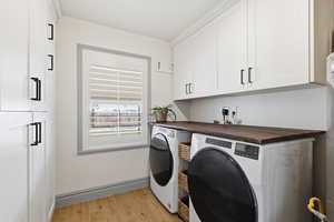 Laundry area with light wood finished floors, cabinet space, and washing machine and dryer