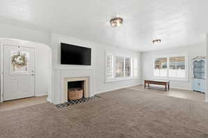 Unfurnished living room featuring a textured ceiling, light carpet, and a fireplace with flush hearth