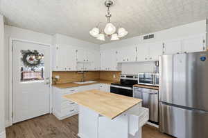 Kitchen featuring stainless steel appliances, a chandelier, light wood-style flooring, and white cabinetry