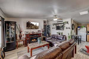 Living area featuring wood finish floors, ceiling fan, and a warm lit fireplace