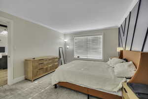 Bedroom with ornamental molding and light colored carpet