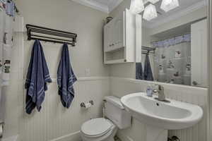 Bathroom with a wainscoted wall, crown molding, and shower / tub combo with curtain