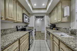 Kitchen with stainless steel appliances, ornamental molding, light stone counters, light wood finish cabinetry, and a raised ceiling