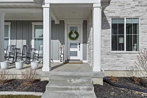 Doorway to property featuring board and batten siding, stone siding, and a porch