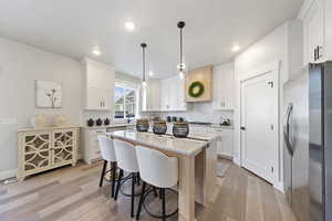 Dual tone kitchen with light stone counters, a kitchen island, stainless steel appliances, a breakfast bar area, and hanging light fixtures