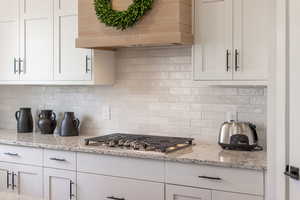 Kitchen featuring white cabinets, light stone counters, stainless steel gas stovetop, and backsplash