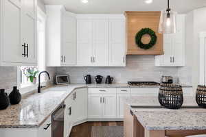 Kitchen featuring light stone countertops, white cabinetry, ventilation hood, and backsplash