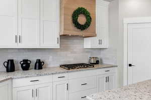 Kitchen with white cabinetry, light stone counters, tasteful backsplash, and stainless steel gas stovetop