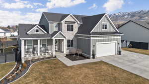 View of front of home with board and batten siding, a standing seam roof, a porch, concrete driveway, and stone siding