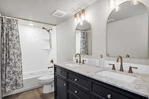 Full bathroom with double vanity, shower / bath combo, and dark wood-style floors