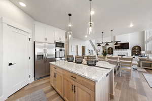 Kitchen featuring light stone counters, stainless steel appliances, hanging light fixtures, light wood-style flooring, and open floor plan