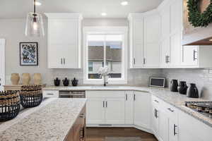 Kitchen featuring light stone countertops, pendant lighting, dark wood-style floors, exhaust hood, and dual tone cabinetry