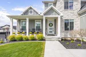 View of exterior entry featuring board and batten siding, stone siding, covered porch, and a yard