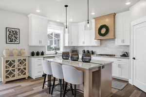 Two tone kitchen with light stone counters, a breakfast bar area, a center island, hanging light fixtures, and tasteful backsplash