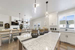 Kitchen featuring light stone counters, decorative light fixtures, a fireplace, light wood finished floors, and open floor plan