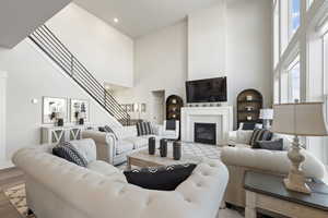 Living room with a high ceiling, a glass covered fireplace, wood finished floors, built in shelves, and recessed lighting