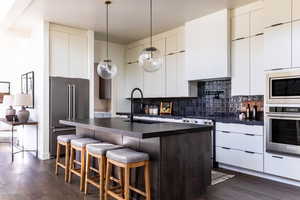 Two tone kitchen featuring stainless steel appliances, decorative light fixtures, dark wood-style floors, a kitchen breakfast bar, and two tone cabinetry