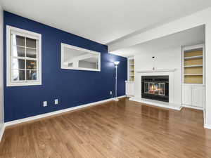 Unfurnished living room with built in features, a glass covered fireplace, and wood finished floors