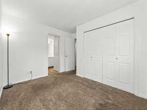 Unfurnished bedroom featuring carpet flooring, a closet, and ensuite bath