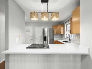 Kitchen with stainless steel fridge, hanging light fixtures, a peninsula, and black electric stovetop