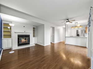 Unfurnished living room featuring a tiled fireplace, dark wood-style flooring, a ceiling fan, and built in features