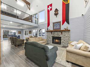 Living room with wood walls, a stone fireplace, hardwood / wood-style floors, and a high ceiling
